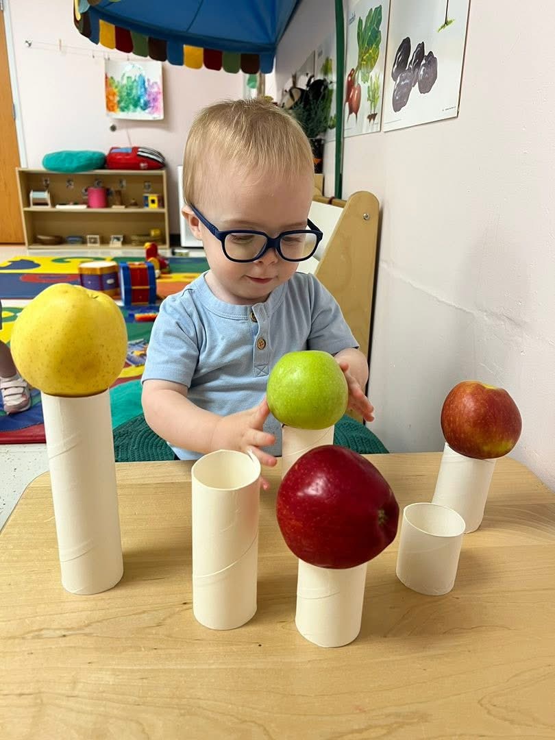 A toddler balancing apples on paper tubes.
