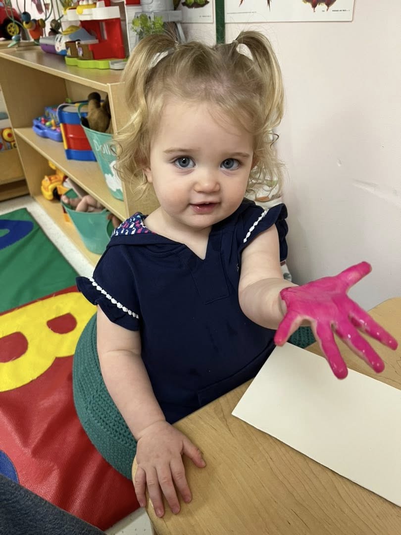A toddler holding up a hand covered in pink paint, ready to print onto paper.