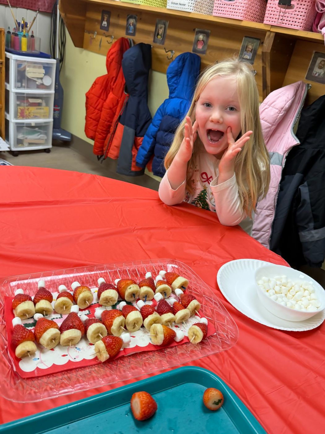 A girl makes an excited face beside a tray of strawberry and banana fruit skewers.