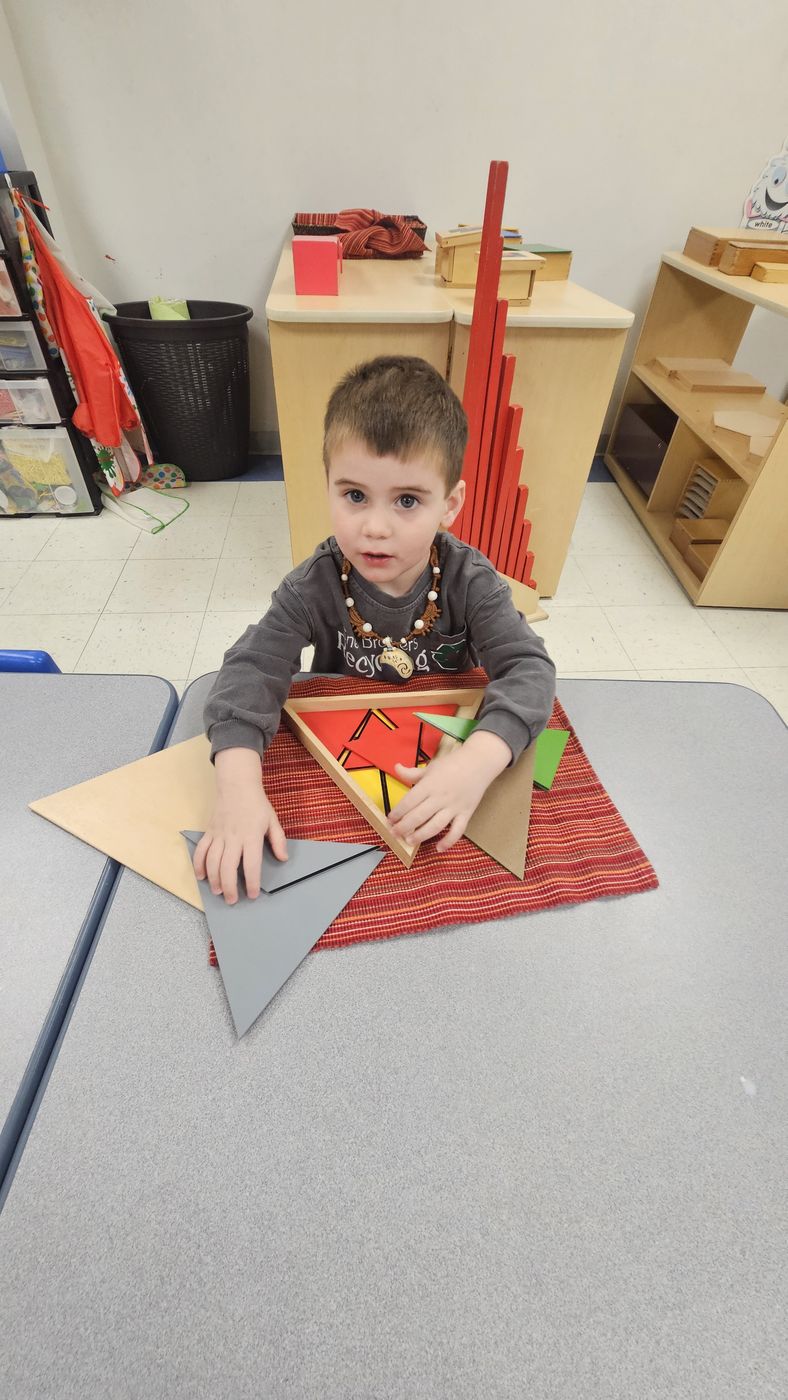 A preschool boy fits wooden triangles together on a red work mat in his Crestwood classroom.