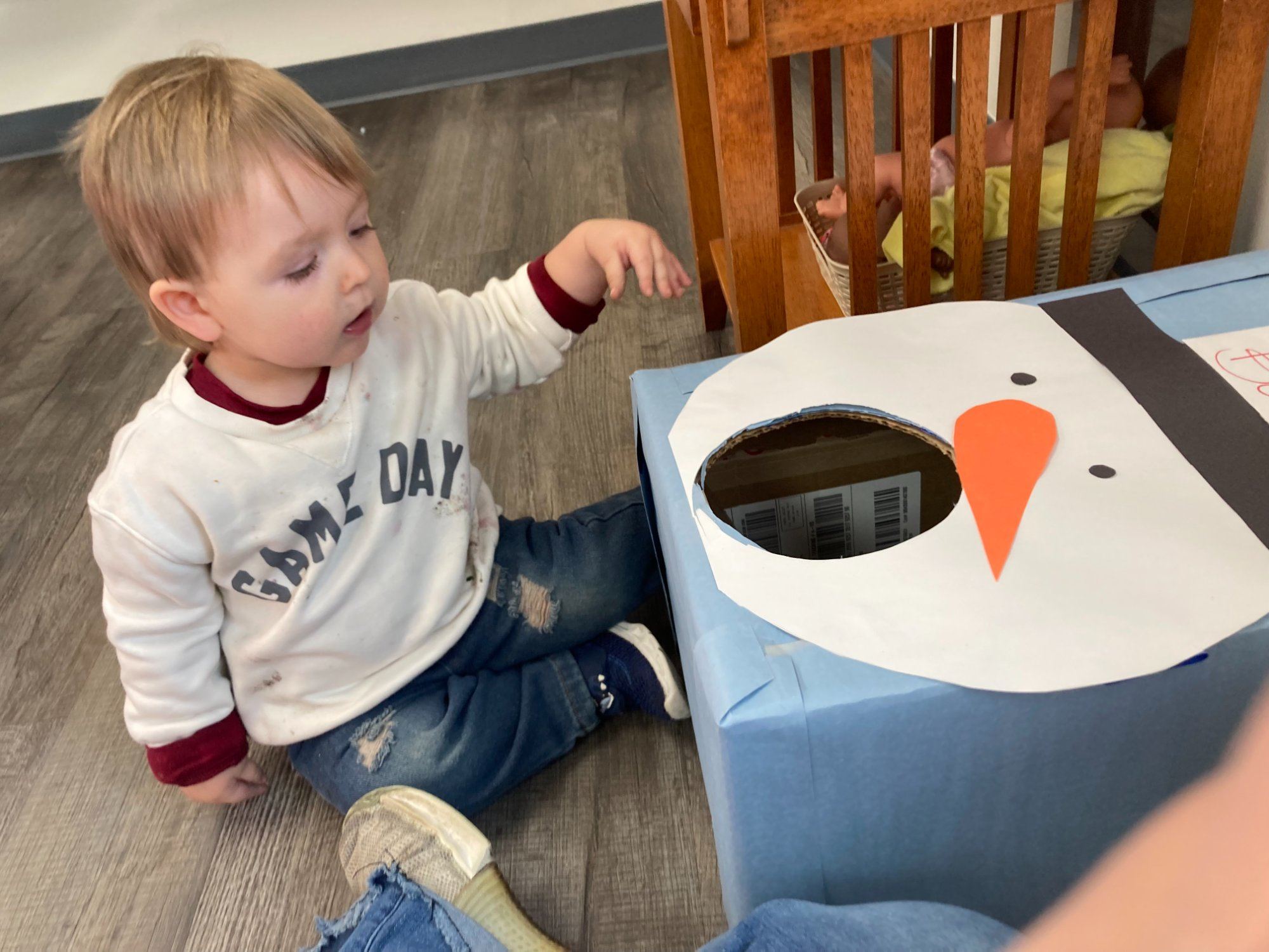 A toddler boy sits on the floor reaching toward a snowman toss game.