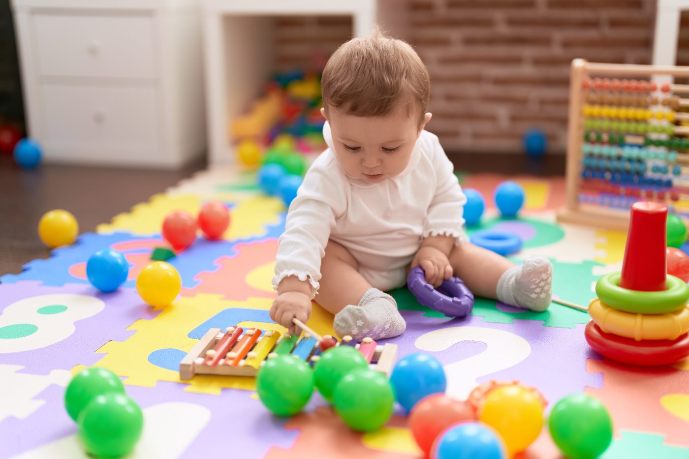 A baby sitting on a colorful play mat, reaching for a wooden xylophone.