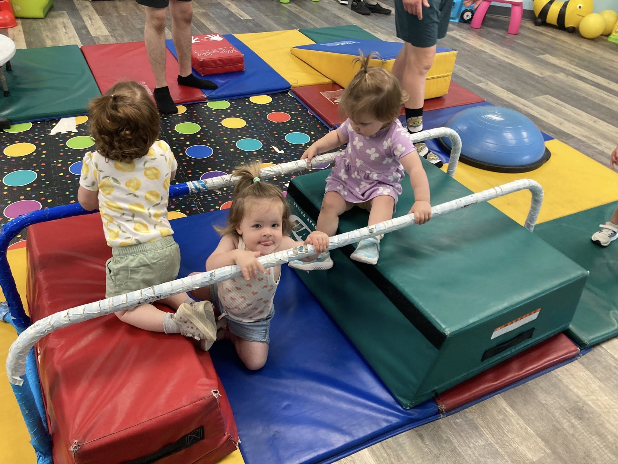 Toddlers climbing padded gym blocks and a balance bar in the indoor gym.