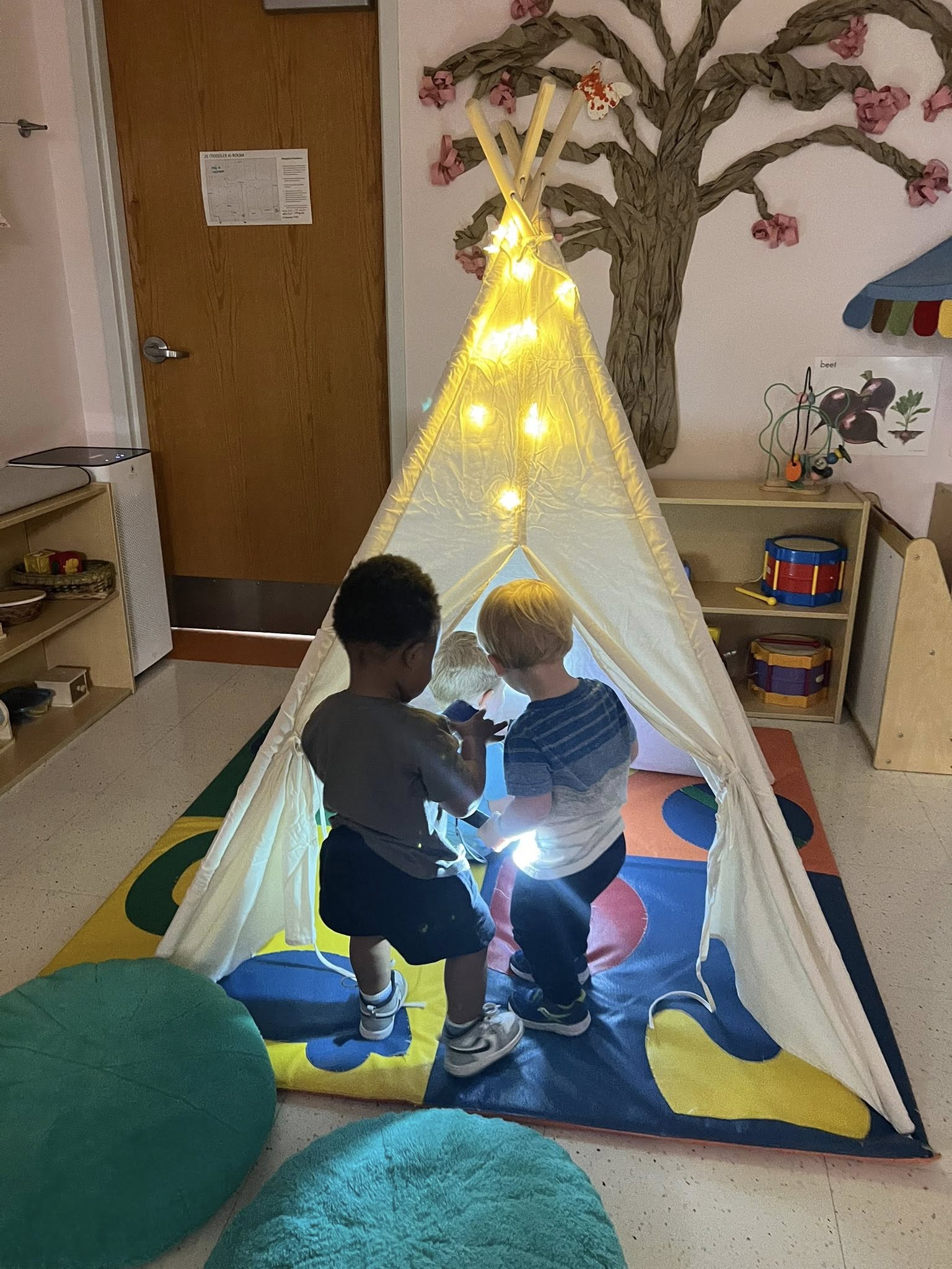 Two toddlers standing inside a fairy-lit play tent in the toddler room.
