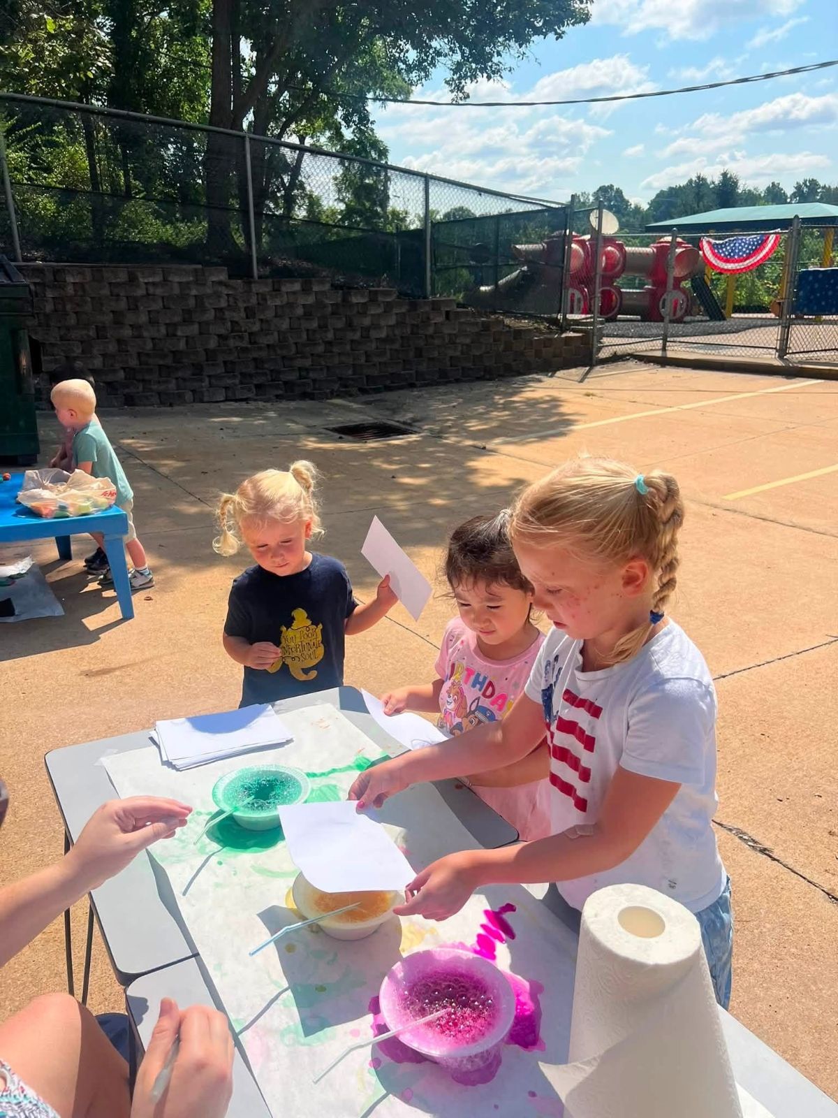 Children doing summer crafts at a table outdoors.