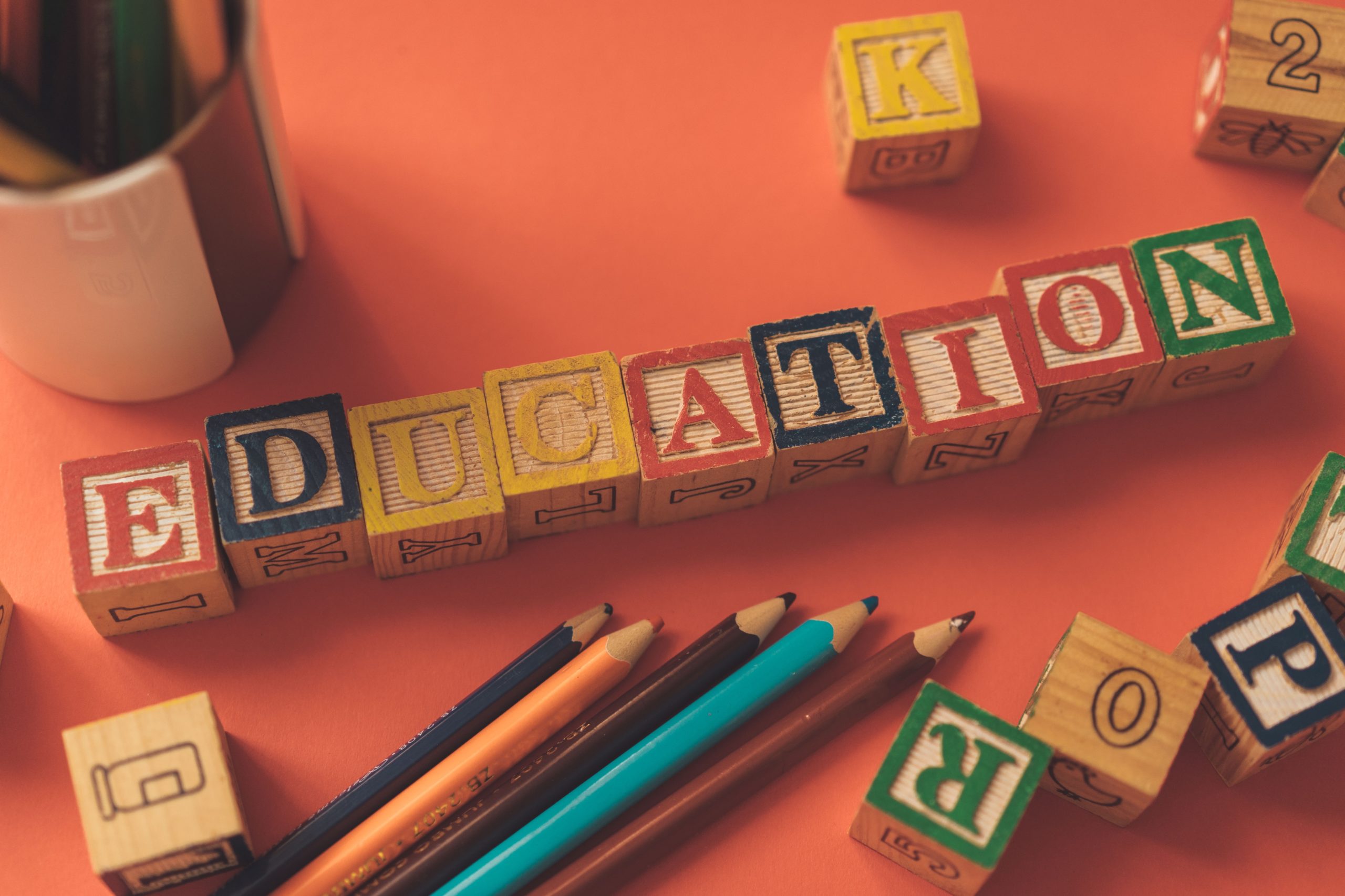 colored pencils next to alphabet blocks on a table spelling out the word education