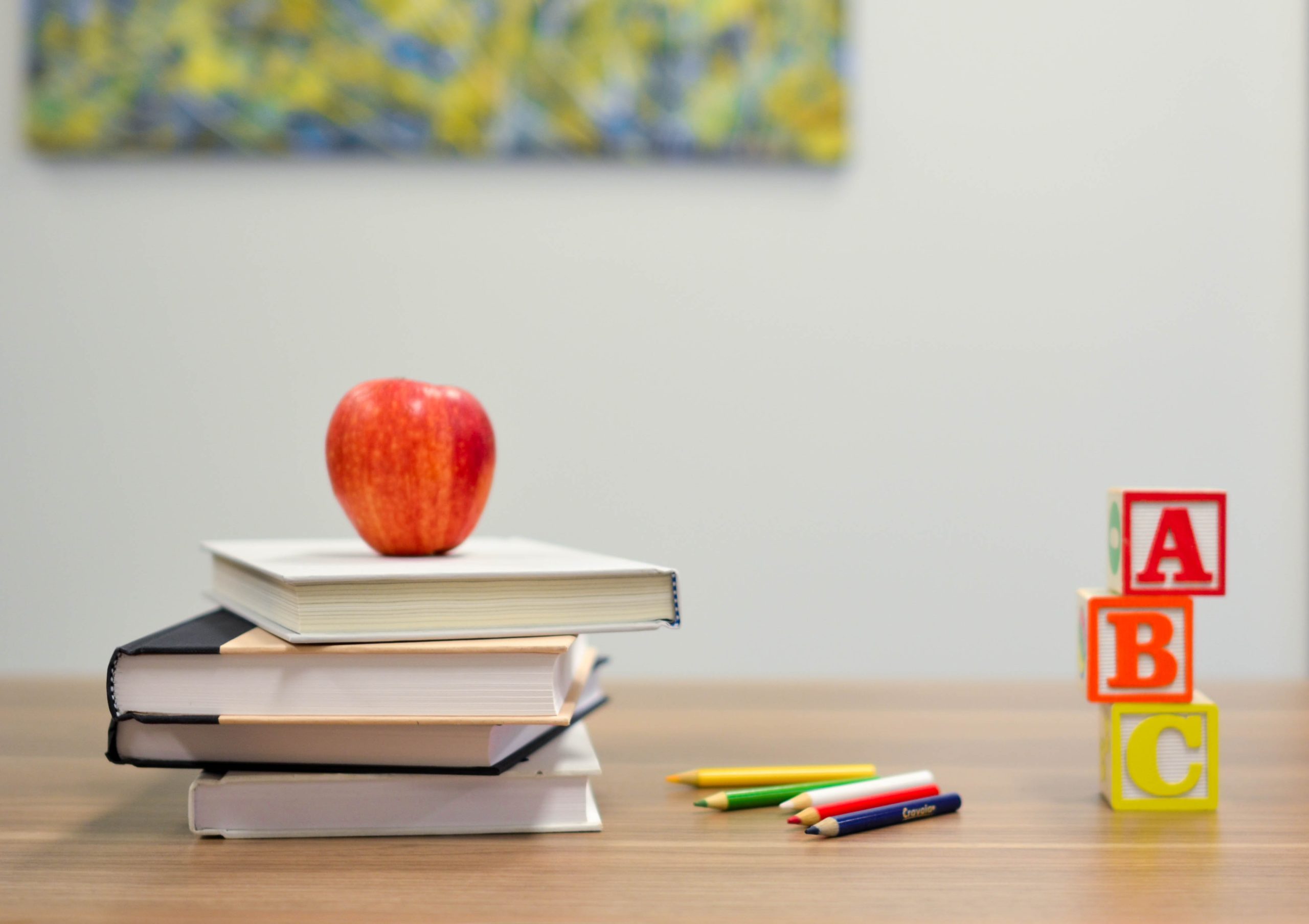 an apple on a stack of books on a classroom desk with colored pencils and alphabet blocks
