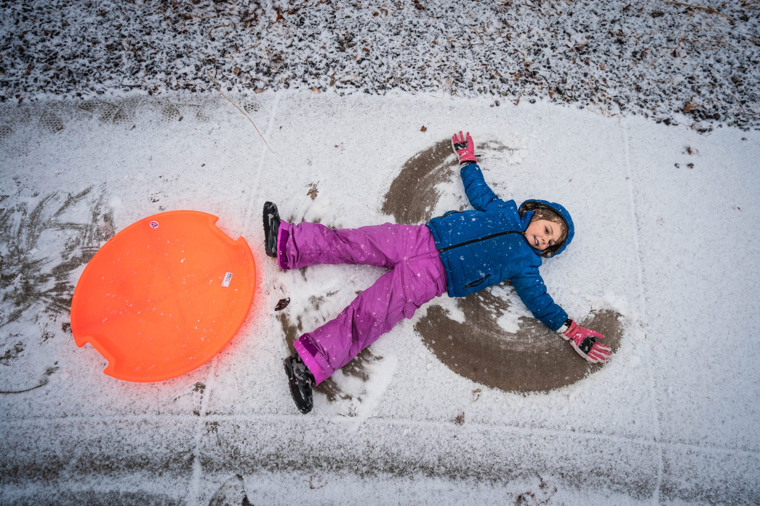 a child making a snow angel next to an orange sled